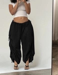 Detail of loose black parachute pants with adjustable drawstring hem and side ruched texture