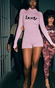 Detail of zip-up long sleeve rompers in pink and camo print with 'body' text logo
