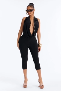 Detail of deep V-neckline with gold studs on a black sleeveless halter jumpsuit