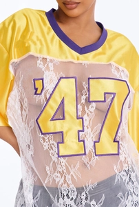 Detail of sheer white floral lace panels and purple V-neck on a yellow satin sports jersey