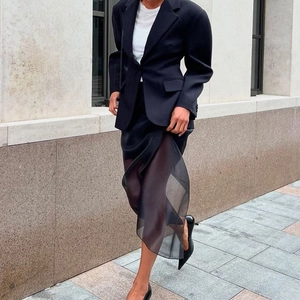 Detail view of a black blazer paired with a sheer mesh paneled midi skirt in high-end fabric
