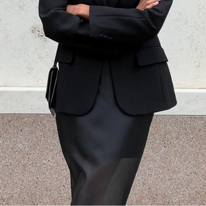 Detail shot of sleek black satin midi skirt paired with a tailored blazer and mini bag