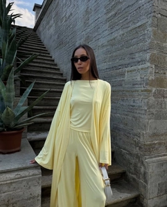 Detail of light yellow knit three-piece set featuring a long cardigan and wide-leg trousers