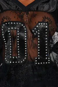 Close-up of black floral lace top featuring a glossy 01 applique with silver rhinestone trim