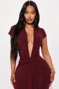Détail du décolleté en V plongeant et du nœud à la taille sur la robe moulante bordeaux