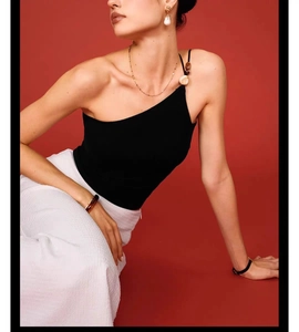 Detail of black one-shoulder yoga sports bra paired with white trousers on red backdrop