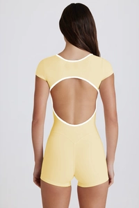 Detail of light yellow yoga bodysuit featuring an open back design with white piping detail
