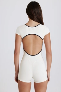 Detail of the open back design with black trim on a cream-colored yoga bodysuit