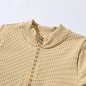 Détail macro du tissu en maille côtelée et du col demi-zippé sur un haut de sport beige