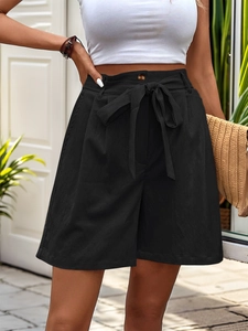 Detail view of high-waisted black shorts featuring a bow tie waist and button closure