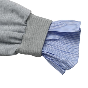 Détail du poignet d'un sweat gris avec superposition de chemise à rayures bleues et bord-côte