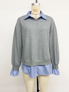 Détail du sweat gris montrant le col de chemise superposé et l'ourlet à rayures bleues