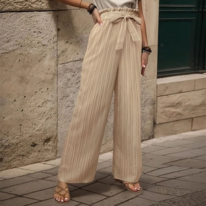 Dettaglio dei pantaloni beige a pieghe con vita alta paperbag e nastro a fiocco in vita