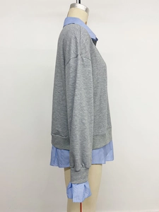 Détail d'un sweat gris avec col et poignets de chemise rayés superposés sur un mannequin