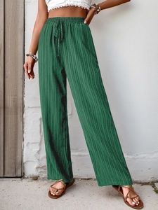 Detail of dark green pleated wide-leg pants with elastic drawstring waist and vertical texture