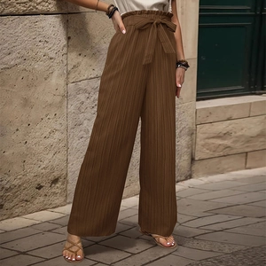 Dettaglio dei pantaloni a gamba larga a vita alta con pieghe verticali e fiocco in vita