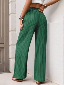 Detailed macro view of the dark green pleated texture and elastic waist of wide-leg trousers