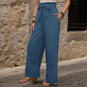 Dettaglio dei pantaloni blu a gamba larga a vita alta con tessuto plissettato e fiocco
