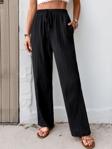 Detail view of black pleated wide-leg trousers with elastic drawstring waist and side pockets