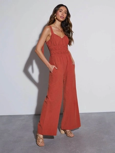 Detail view of rust red smocked waist jumpsuit with thin straps and wide leg cut