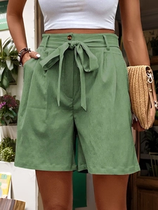 Detail of high-waisted green cotton shorts with a tie-belt and amber button accent