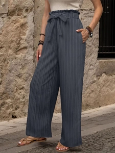 Dettaglio dei pantaloni a vita alta con cintura a fiocco e trama plissettata fine