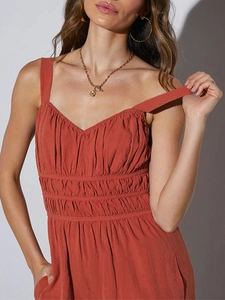 Detail view of rust red jumpsuit featuring thin straps and elastic smocked waist texture
