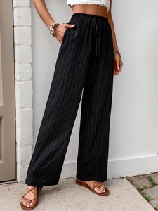 Detail of high waisted black wide leg pants featuring pleated texture and drawstring waist