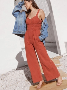Detail of high-waist pleated jumpsuit in brick red with wide-leg cut and denim jacket