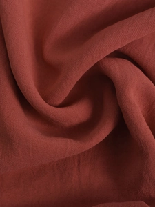 Macro texture of brick red summer jumpsuit fabric showing fine weave and soft drape