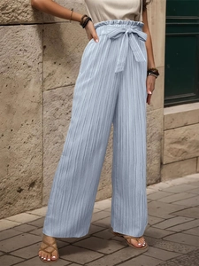 Dettaglio dei pantaloni plissettati azzurri a gamba larga con vita alta e fiocco annodato