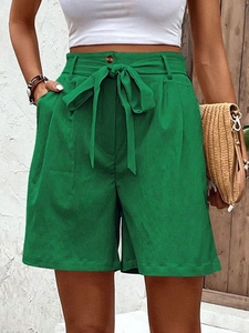 Close-up of bright green high-waisted shorts with bow belt and cotton linen texture