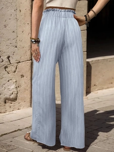 Dettaglio vita alta a sacchetto con elastico arricciato su pantaloni larghi celesti