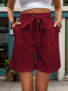 Detail of high-waist burgundy shorts with bow-tie belt and vintage brown buttons