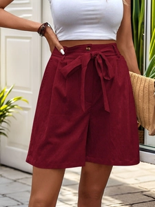 Detail of high-waisted burgundy shorts featuring a bow tie waist and corduroy texture