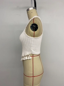Detailed side view of white cable knit crop top featuring tassel fringe and side slit detail