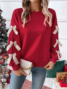 Detail of red crewneck sweatshirt with white 3D bows on sleeves in a festive Christmas setting