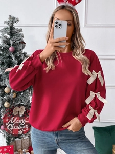 Detail of red crewneck sweatshirt with white satin bows on sleeves for Christmas