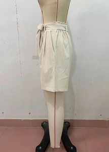 Detail view of high waisted beige paperbag shorts with side pockets and a ribbon tie belt
