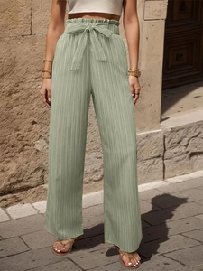 Dettaglio di pantaloni larghi a pieghe a vita alta con fiocco in colore verde salvia