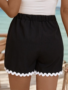 Detail view of the elastic waistband and white scalloped trim on black beach shorts