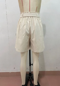 Rear view of beige high-waisted paper-bag shorts featuring an elastic pleated waistband