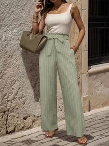 Dettaglio dei pantaloni a gamba larga a vita alta con cintura a fiocco e trama a pieghe