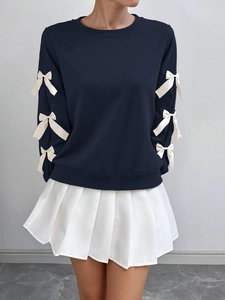 Detail of navy sweatshirt with white bow accents and pleated skirt ensemble