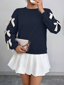 Detail of dark navy sweatshirt sleeves featuring decorative cream satin bows and thick fabric