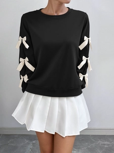 Detail of black crewneck sweatshirt featuring white decorative bows on long sleeves