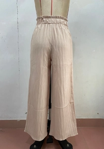 Dettaglio dei pantaloni a gamba larga plissettati beige chiaro con vita alta elasticizzata