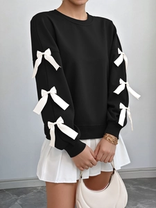 Close-up of black sweatshirt sleeves featuring white satin bow details and knit texture