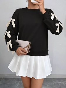 Detail of black crewneck sweatshirt featuring white silk bows and pleated white skirt