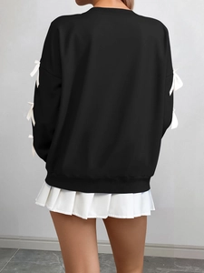 Detail of black crewneck sweatshirt featuring white bow accents on long sleeves back view